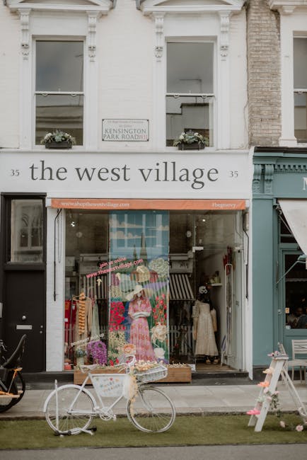 The image shows the exterior of a boutique shop named 'the west village' located at 35 Kensington Park Road, with two large upper windows adorned with flower boxes. The shop's large glass display wind