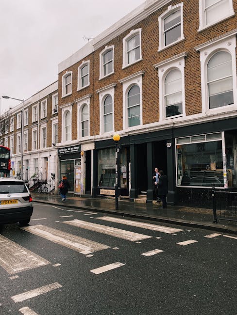 The image depicts a row of commercial storefronts on a street corner in Kensington High Street, West Kensington, with a focus on the exterior facades of the shops. The buildings are multi-story, featu